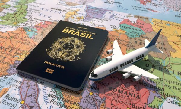 Foto de um passaporte brasileiro, cor azul. Atrás o mapa mundi.