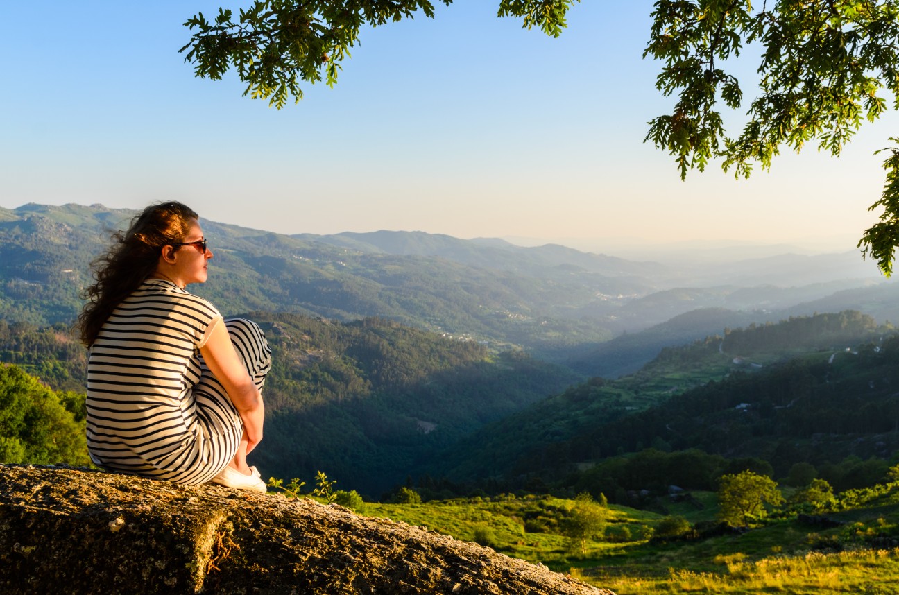 Imagem de uma mulher de costas em um morro observando a natureza